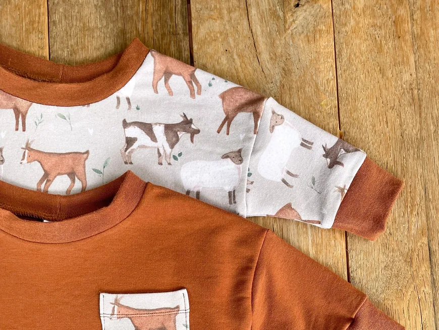 Two rust-orange baby sweaters, one with a goat print and one with a goat pocket