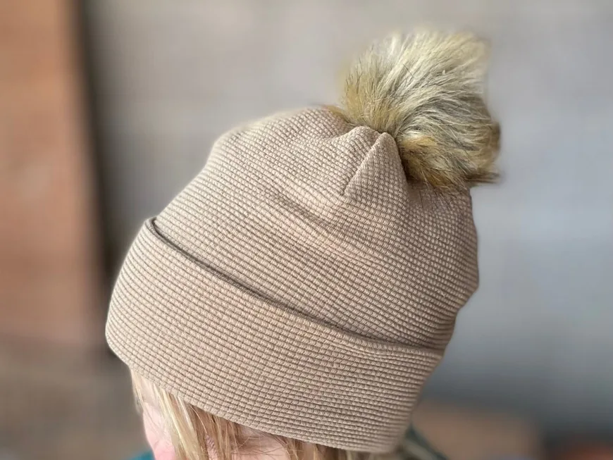 A child wearing a tan slouchy beanie with a fluffy pom-pom